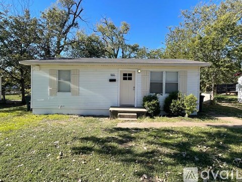 A small white house with a porch and a tree in front.