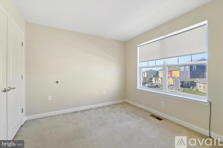A room with a carpeted floor, a door, and a window showing a view of a residential area.