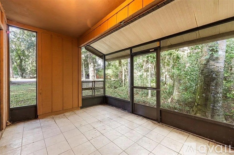 A room with a view of a forest through large windows.