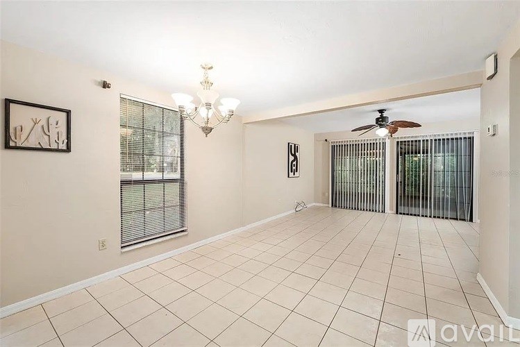 A spacious room with a chandelier, two windows with blinds, and a ceiling fan.