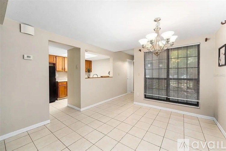 A spacious living room with a chandelier and a window with blinds.