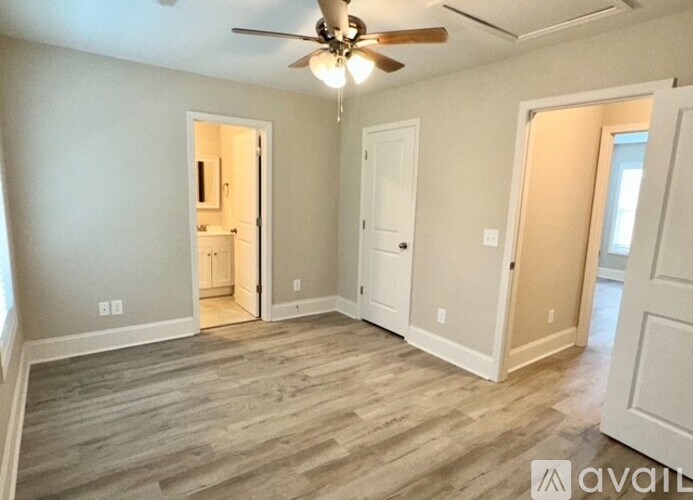 A room with a ceiling fan and light, wooden floors, and white walls with a doorway leading to another room.