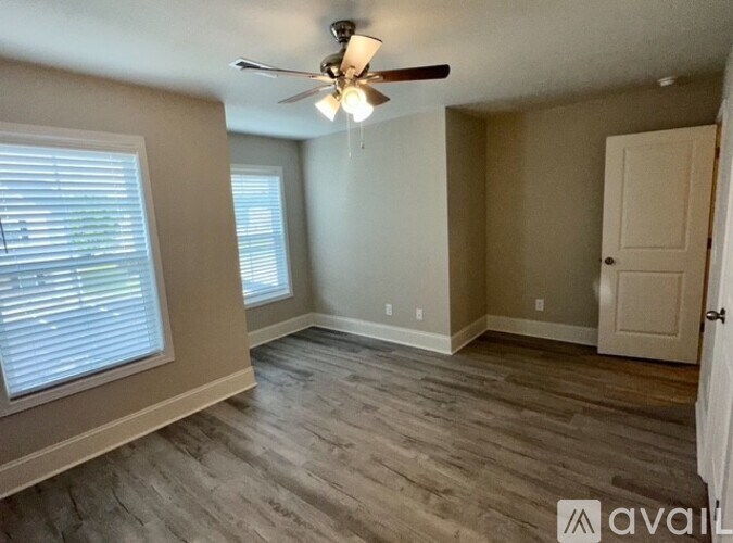A room with a ceiling fan and light, two windows with blinds, and a door.