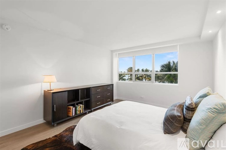 A bedroom with a bed, a dresser with a lamp, and a window overlooking a beach.