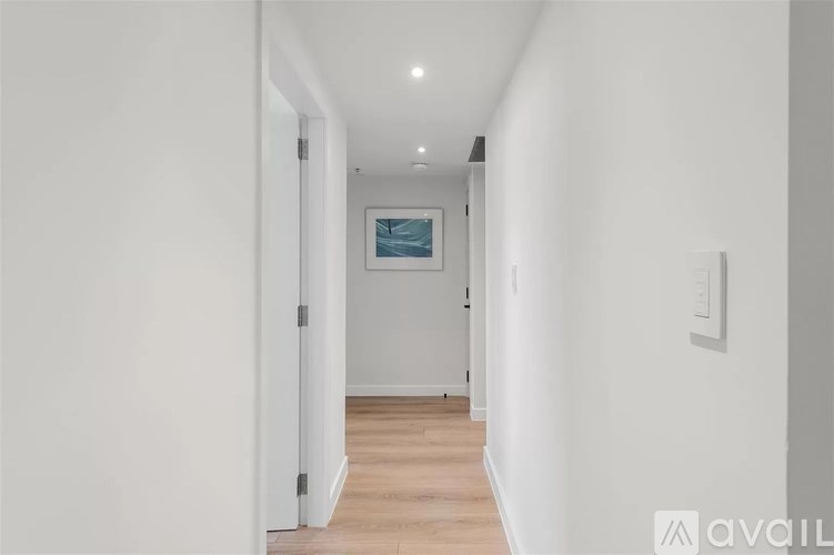 A long white hallway with a painting on the wall and a door on the left.