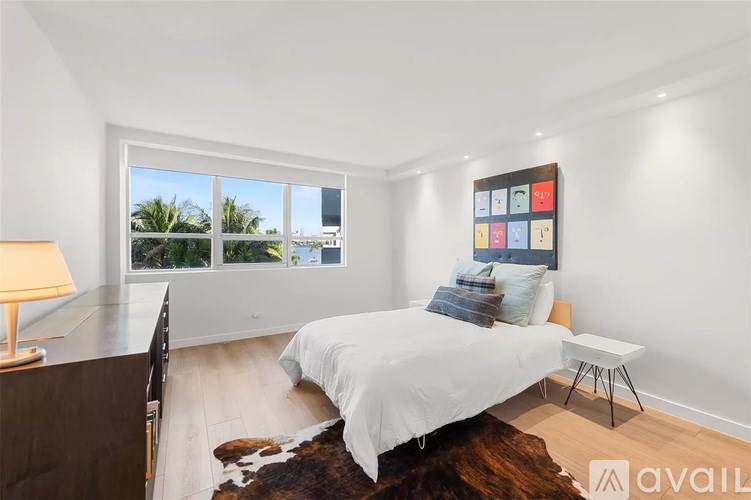 A bedroom with a large bed, a cowhide rug, and a window with a view of palm trees.