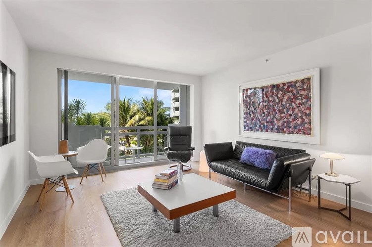 A living room with a black leather couch, a coffee table, and a large window overlooking a balcony.
