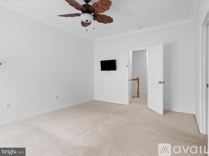 A room with a ceiling fan and a flat screen TV mounted on the wall.