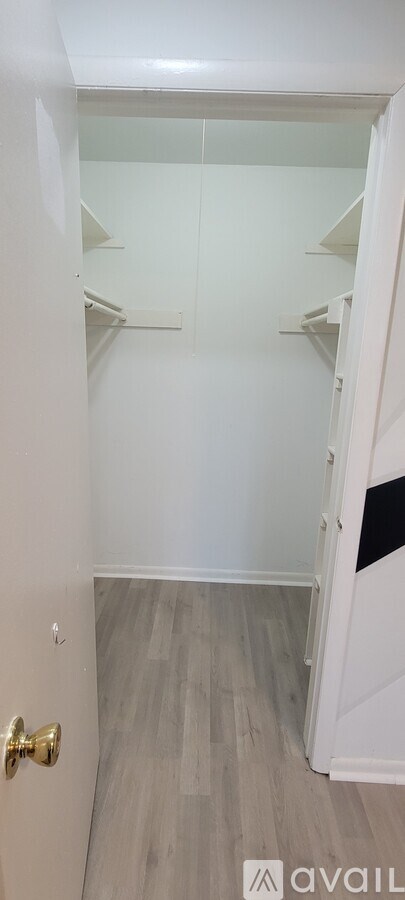 A white door with a gold handle is open to a hallway with white walls and wood flooring.