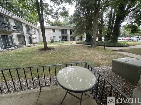 A patio with a table and chairs overlooking a grassy area with trees and apartment buildings.