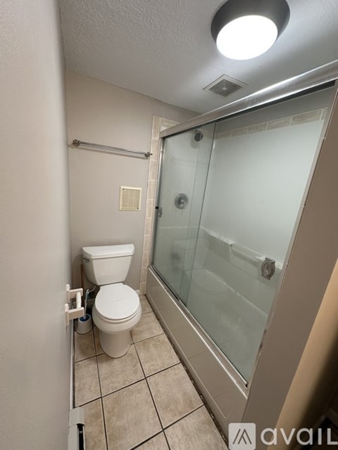 A bathroom with a toilet, glass shower door, and a white wall.