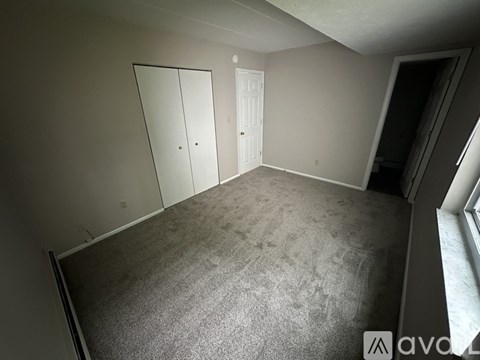 A room with grey carpet and white walls, featuring a white door and a white wardrobe.