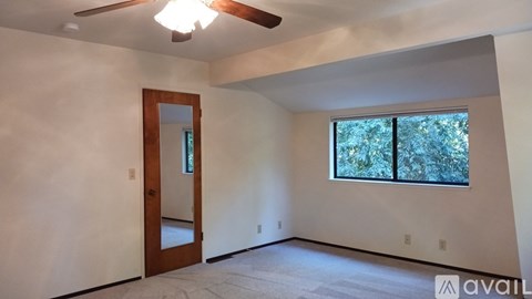A room with a ceiling fan and a window overlooking trees.