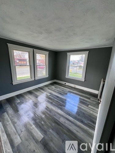 A room with grey wooden flooring and three windows.