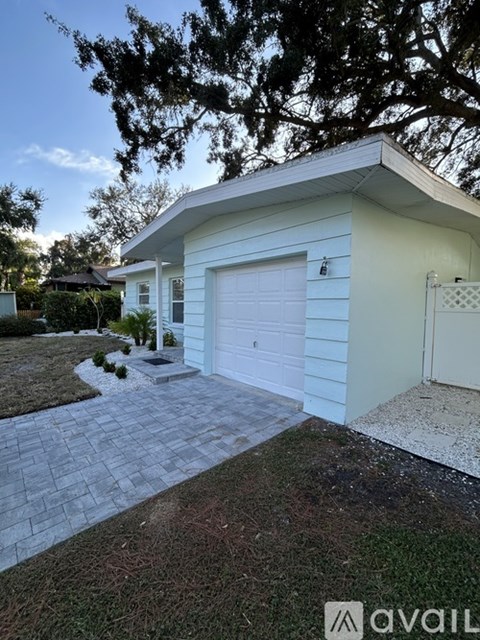 A white house with a garage door and a tree in front.