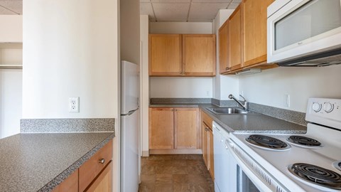 Kitchen with light wood cabinets, speckled countertops, white appliances, and tile flooring in a compact galley layout.