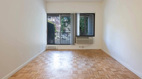 Living room with parquet flooring and large sliding windows leading to a private balcony at 929 Mass Apartments.