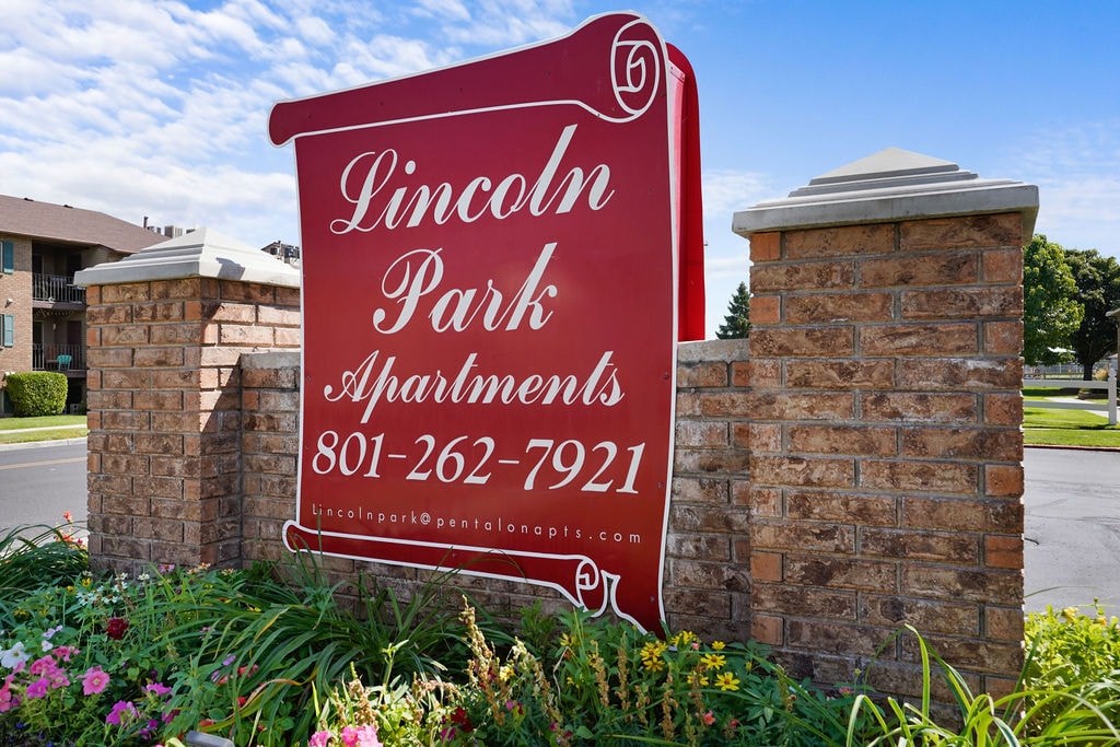 A sign for Lincoln Park Apartments is displayed in front of a brick wall.