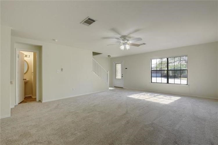 A spacious room with a carpeted floor, a ceiling fan, and a window with blinds.