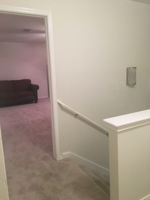 A hallway with a white wall and a white railing.