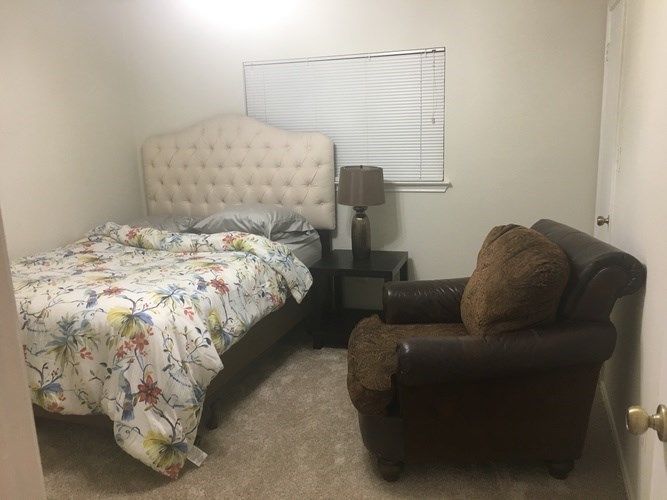 A bed with a floral comforter sits next to a brown leather chair in a room.