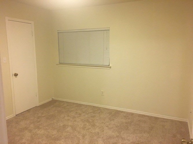 A room with a carpeted floor and a window with blinds.
