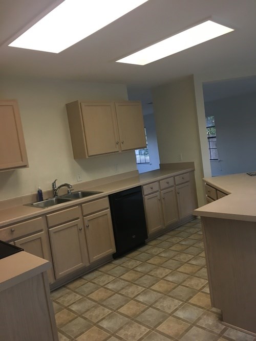 A kitchen with a black dishwasher and brown cabinets.