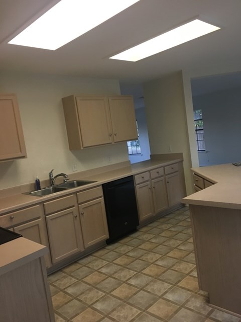 A kitchen with a black dishwasher and brown cabinets.