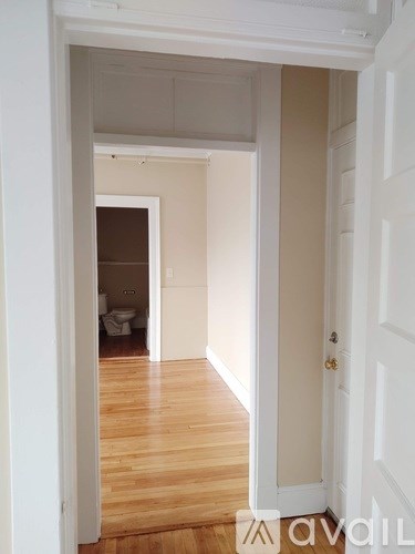 A hallway with a door on the right and a toilet visible in the background.