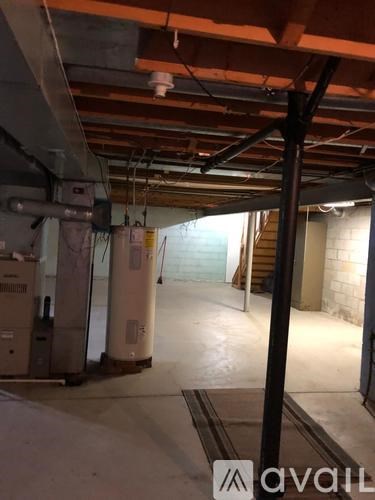 A room with a concrete floor and a ceiling with exposed pipes and wooden beams.