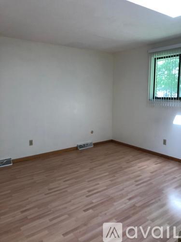 A room with wooden flooring and a window with a view of trees outside.