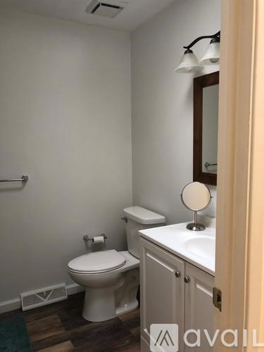 A white toilet sits in a small bathroom with a white vanity and a mirror.