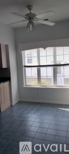 A room with a ceiling fan and large windows.