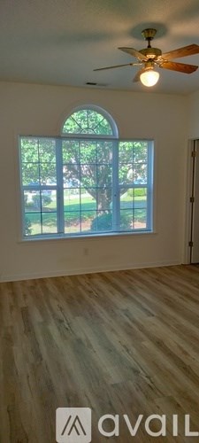 A room with a ceiling fan and a window overlooking a green lawn.