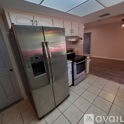 A stainless steel refrigerator is in a kitchen with white cabinets.