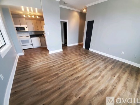 A spacious room with wooden flooring and a kitchen area in the background.