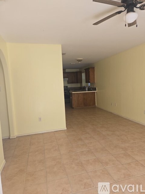 A room with a ceiling fan and a kitchen area in the background.