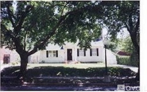 A white house with a black door is surrounded by trees.