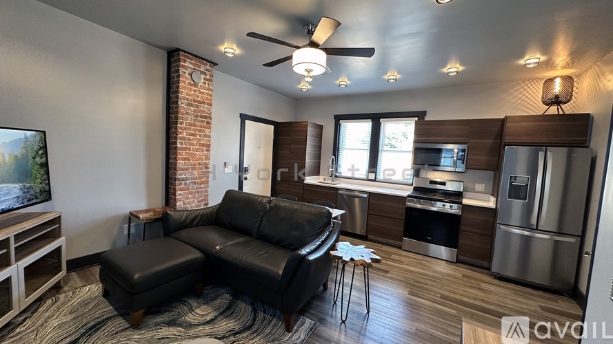 A modern living room with a black leather sofa and a kitchen area in the background.