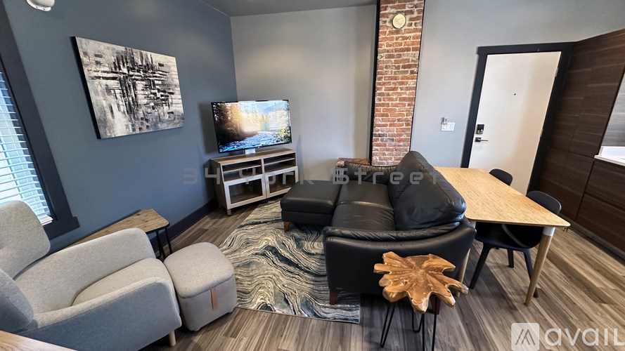A living room with a grey couch, a black ottoman, a wooden table, and a TV on a stand.