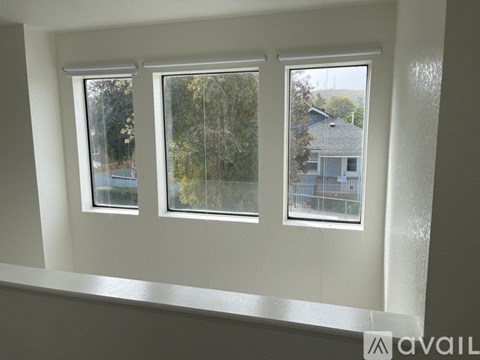 Three windows in a white room with a view of trees and a house.