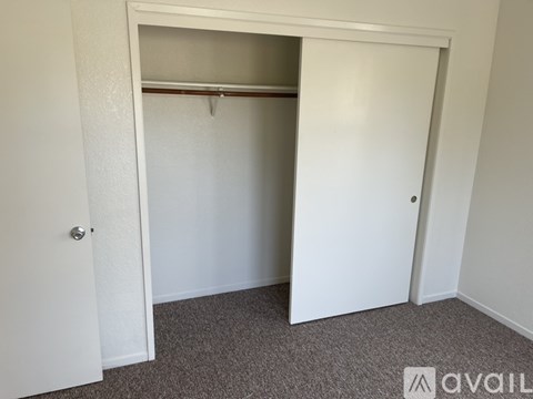 A white door is open to reveal a closet with a shelf and a carpeted floor.