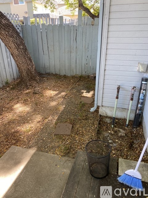 A backyard with a white fence and a broom leaning against it.