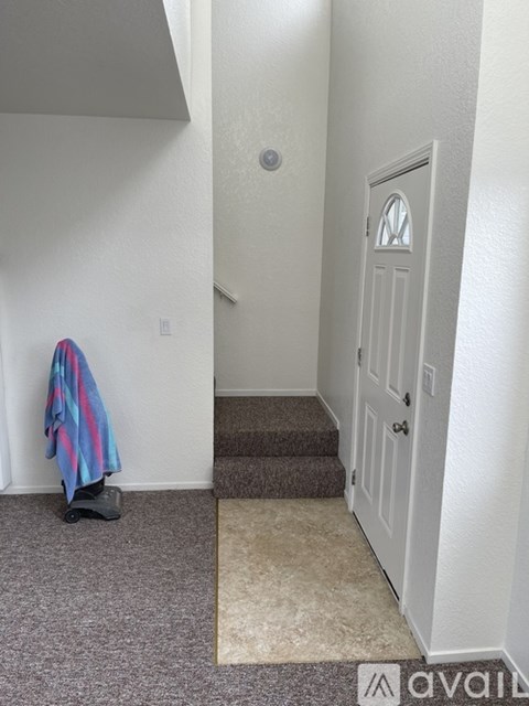 A hallway with a carpeted floor, a door, and a coat hanging on the wall.