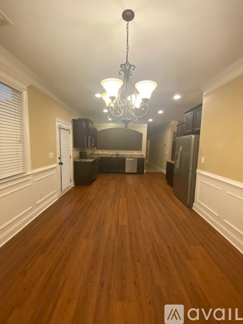 A long hallway with a chandelier and a kitchen in the background.