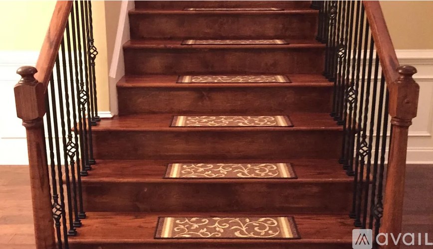 A staircase with a wooden handrail and a patterned rug on the steps.