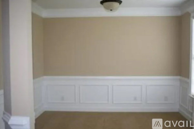 A room with beige walls and white paneling on the bottom.