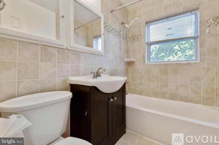 A bathroom with a white tub, sink, and a window.