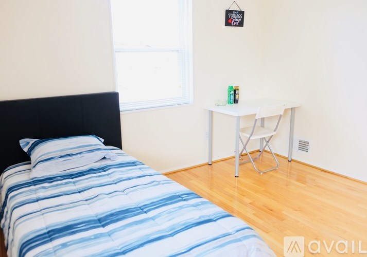 A bed with blue and white striped bedding sits in a room with a small white table and a black clock on the wall.