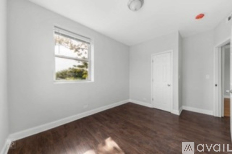 A room with wooden floors and white walls, a window, and a door.